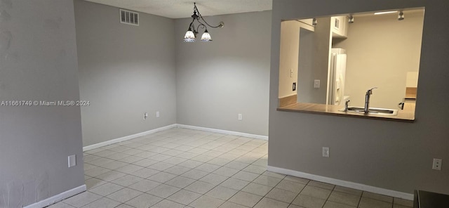 unfurnished dining area with sink, light tile patterned floors, a textured ceiling, and a notable chandelier