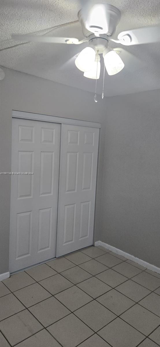 unfurnished bedroom with ceiling fan, a closet, light tile patterned floors, and a textured ceiling