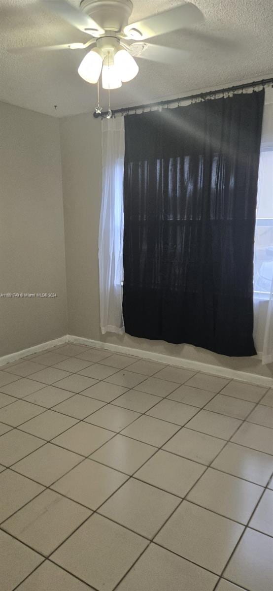 tiled empty room with ceiling fan and a textured ceiling