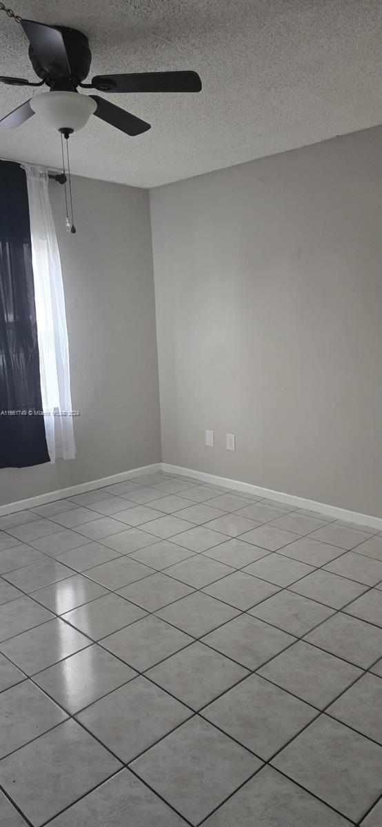 empty room featuring a textured ceiling, ceiling fan, and light tile patterned flooring