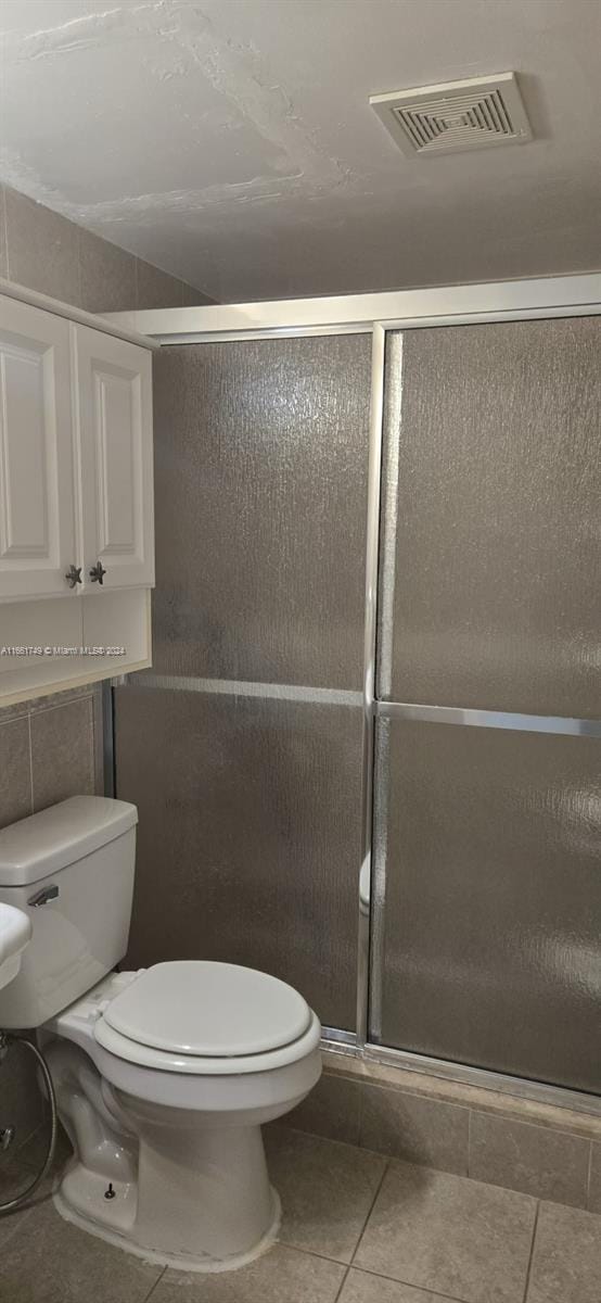 bathroom featuring walk in shower, tile patterned flooring, and toilet