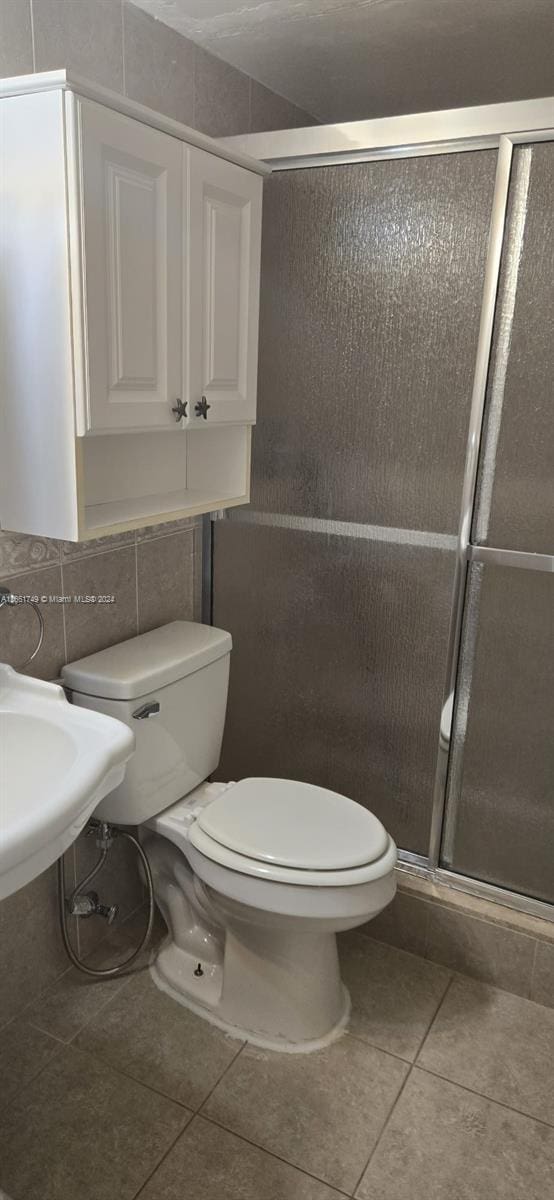 bathroom with tile patterned floors, toilet, a shower with door, and tile walls