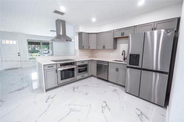 kitchen featuring gray cabinetry, stainless steel appliances, a sink, visible vents, and wall chimney range hood