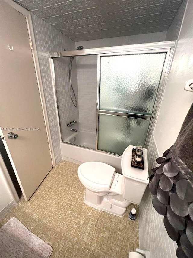 bathroom featuring combined bath / shower with glass door and toilet