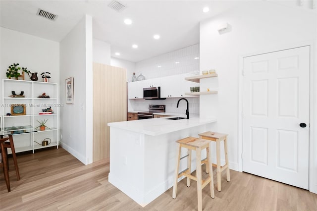 kitchen featuring white cabinetry, kitchen peninsula, stainless steel appliances, light hardwood / wood-style flooring, and sink