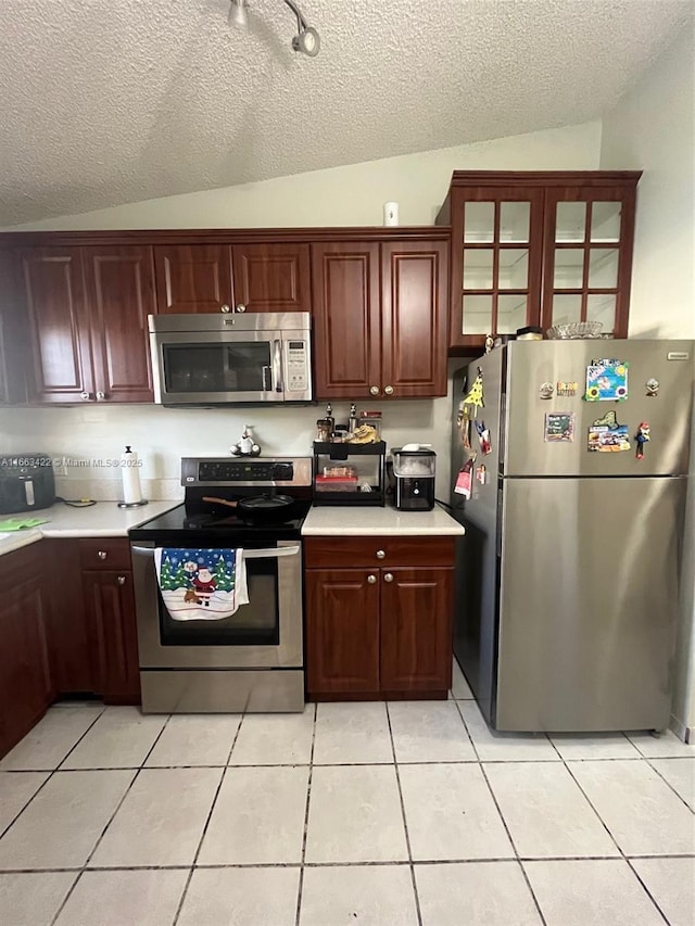 kitchen with light tile patterned flooring, appliances with stainless steel finishes, light countertops, and lofted ceiling