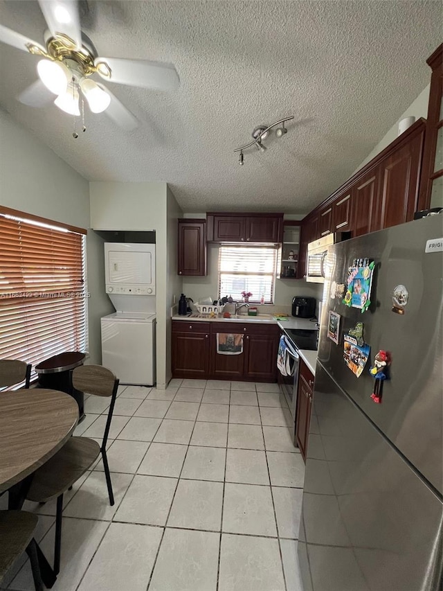 kitchen featuring stacked washing maching and dryer, stainless steel appliances, light countertops, light tile patterned floors, and ceiling fan