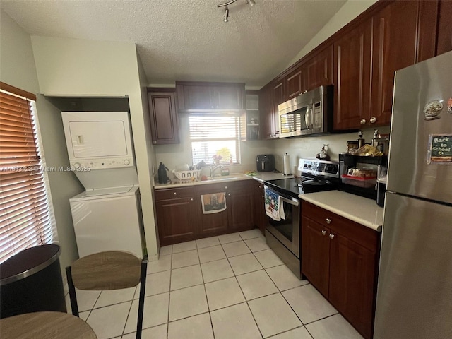 kitchen with light tile patterned flooring, a sink, stainless steel appliances, light countertops, and stacked washer and clothes dryer