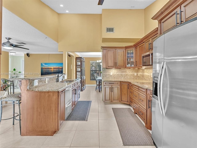 kitchen featuring ceiling fan, light stone counters, light tile patterned floors, appliances with stainless steel finishes, and a kitchen bar