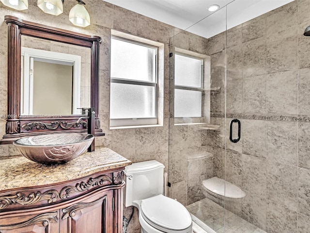 bathroom with tile walls, a shower with shower door, vanity, and toilet