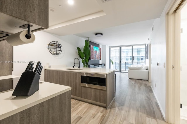 kitchen featuring sink, a wall of windows, kitchen peninsula, oven, and light hardwood / wood-style floors