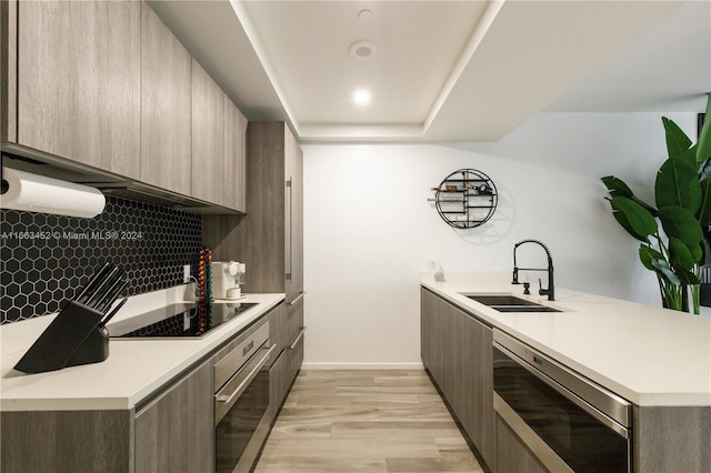 kitchen with sink, light hardwood / wood-style flooring, tasteful backsplash, kitchen peninsula, and stainless steel appliances