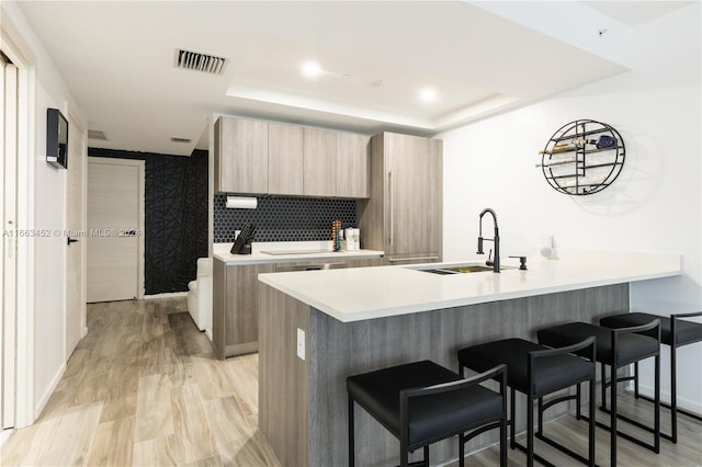 kitchen with a breakfast bar, sink, a tray ceiling, and light hardwood / wood-style flooring