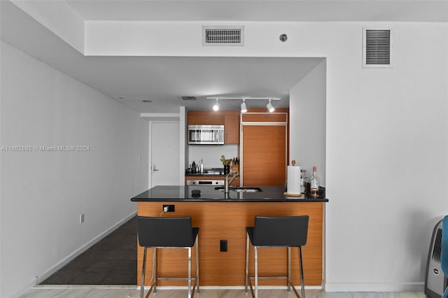 kitchen featuring kitchen peninsula, sink, a kitchen bar, and rail lighting