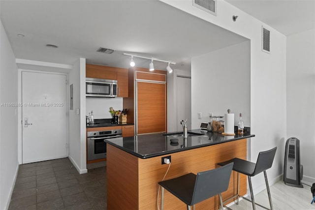 kitchen featuring dark countertops, visible vents, appliances with stainless steel finishes, a sink, and a peninsula