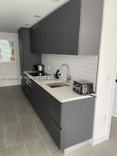 kitchen featuring black electric stovetop, backsplash, light tile patterned floors, and sink