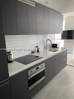 kitchen featuring sink, light tile patterned floors, fridge, black electric cooktop, and stainless steel oven