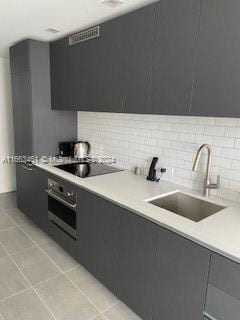 kitchen featuring decorative backsplash, light tile patterned floors, oven, black electric stovetop, and sink