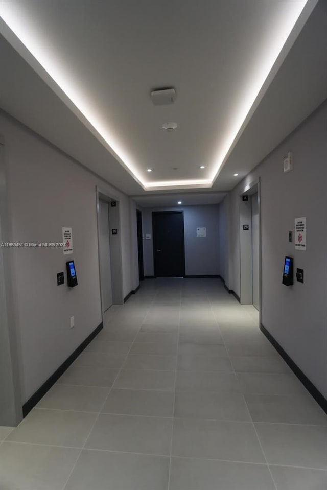 hallway with a tray ceiling, light tile patterned floors, and elevator