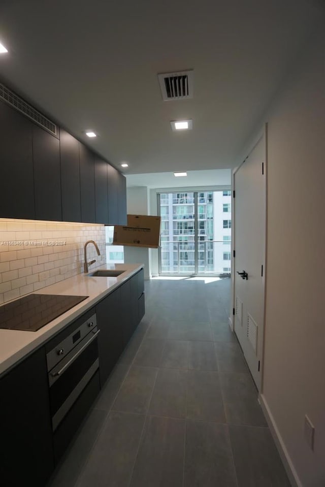 kitchen featuring sink, dark tile patterned floors, tasteful backsplash, black electric cooktop, and stainless steel oven