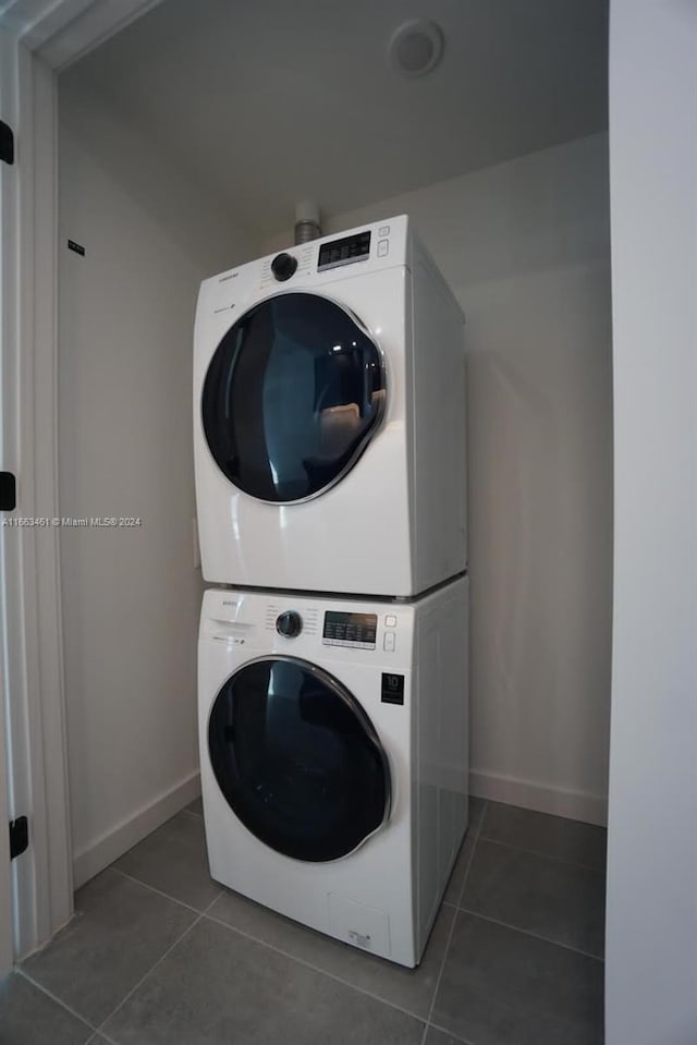 laundry area featuring dark tile patterned flooring and stacked washer / dryer