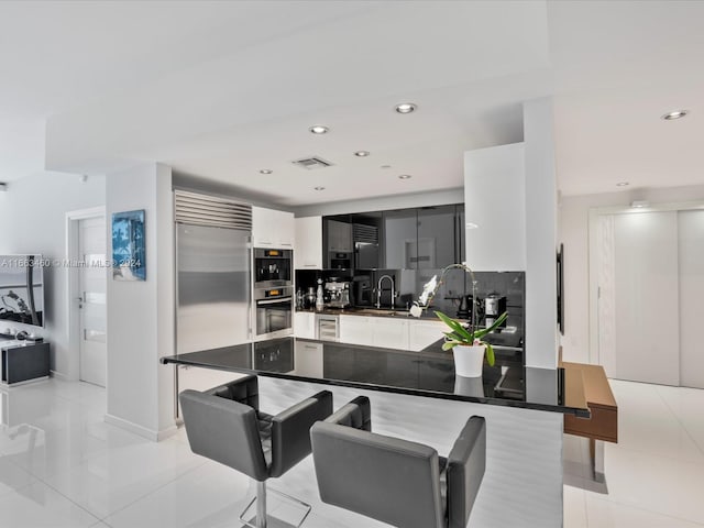 kitchen with built in refrigerator, backsplash, kitchen peninsula, light tile patterned floors, and sink