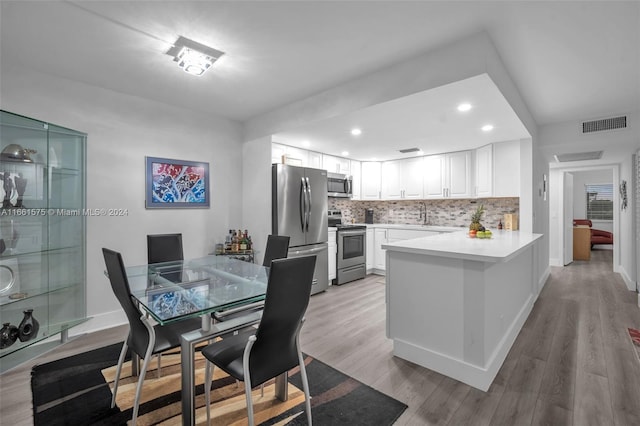 kitchen featuring white cabinetry, backsplash, light hardwood / wood-style floors, kitchen peninsula, and stainless steel appliances