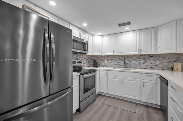 kitchen with sink, backsplash, stainless steel appliances, white cabinets, and light wood-type flooring