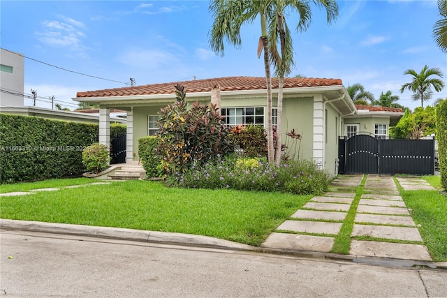 view of front facade with a tile roof, a front yard, stucco siding, and a gate