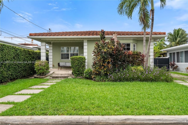 view of front of house featuring a tile roof, a front lawn, stucco siding, and covered porch