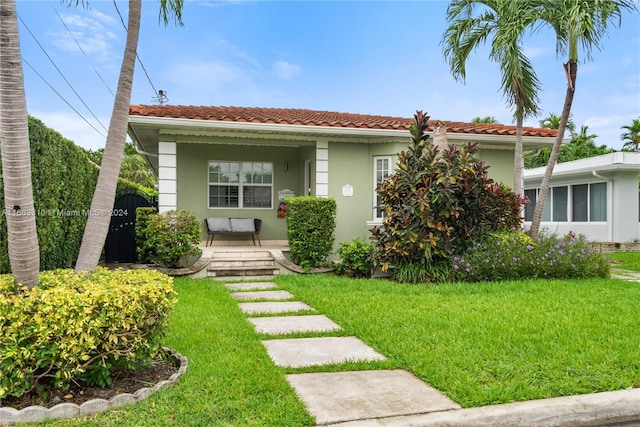 view of front of home with stucco siding, covered porch, a front lawn, and a tile roof