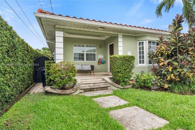view of exterior entry with stucco siding, covered porch, and a lawn