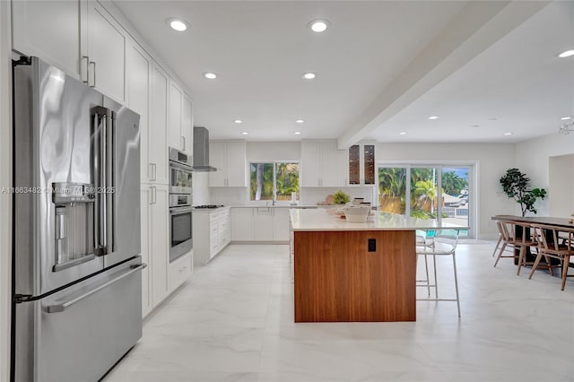 kitchen with backsplash, wall chimney range hood, a kitchen island, white cabinetry, and stainless steel appliances