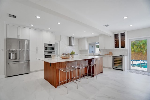 kitchen with white cabinets, wall chimney exhaust hood, a kitchen island, and stainless steel appliances