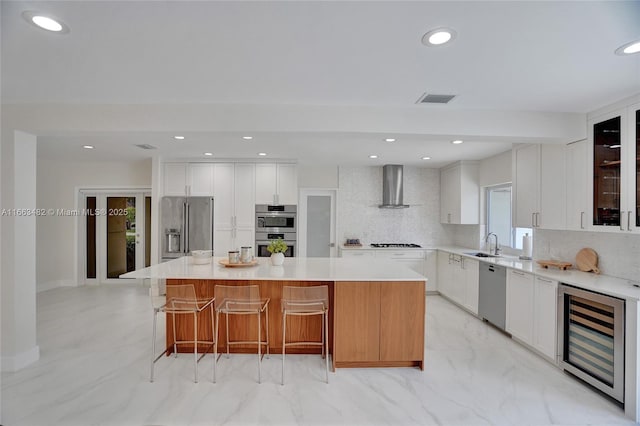 kitchen with a center island, white cabinets, wine cooler, wall chimney exhaust hood, and stainless steel appliances