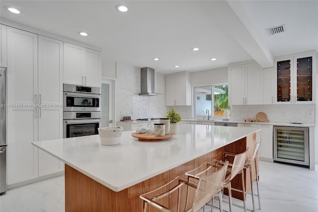 kitchen featuring wine cooler, a center island, white cabinetry, and wall chimney range hood