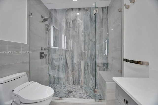 bathroom with vanity, a shower with shower door, tile walls, and toilet