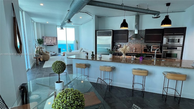 kitchen with pendant lighting, light stone counters, built in appliances, sink, and a kitchen breakfast bar