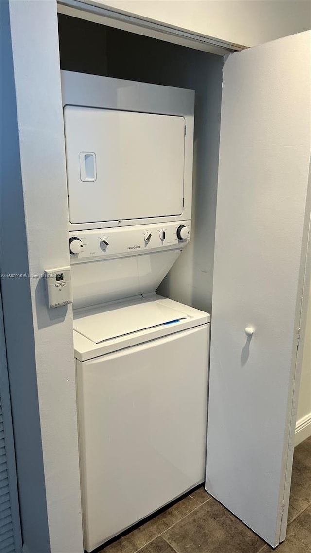 clothes washing area featuring dark tile patterned flooring and stacked washer and dryer