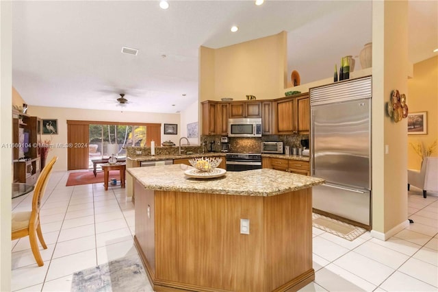 kitchen featuring kitchen peninsula, stainless steel appliances, light tile patterned floors, light stone countertops, and ceiling fan