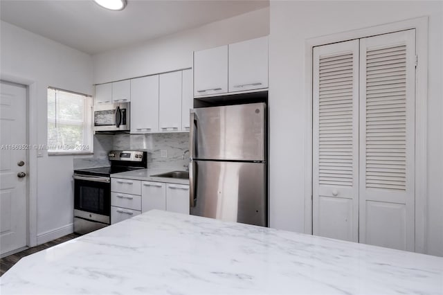 kitchen featuring white cabinetry, dark wood-type flooring, tasteful backsplash, light stone countertops, and stainless steel appliances