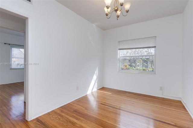 empty room with an inviting chandelier, a healthy amount of sunlight, and hardwood / wood-style floors