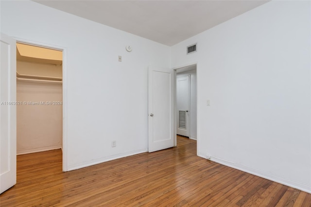 unfurnished bedroom with a spacious closet, a closet, and hardwood / wood-style floors