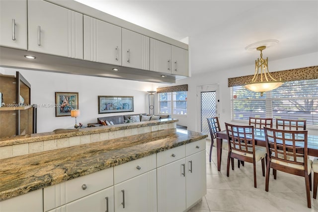 kitchen with white cabinets, dark stone countertops, light tile patterned floors, and decorative light fixtures