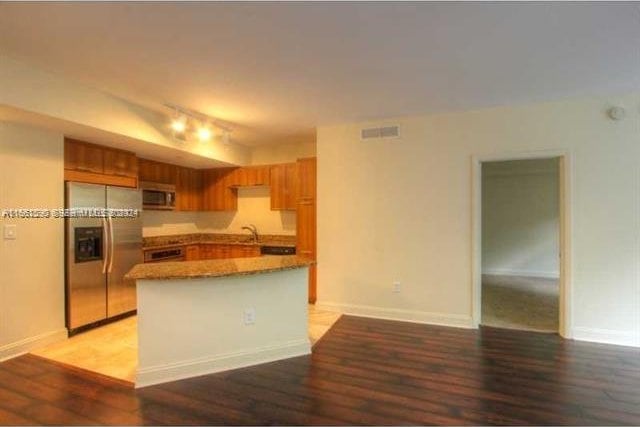 kitchen featuring light stone counters, sink, stainless steel appliances, a center island, and hardwood / wood-style floors