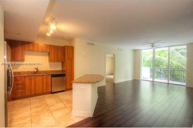 kitchen featuring light stone counters, light wood-type flooring, ceiling fan, stainless steel dishwasher, and sink