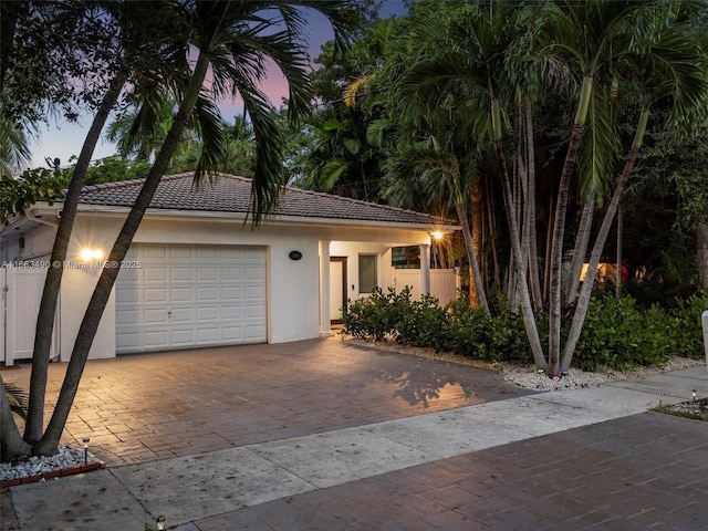 view of front of property with a garage, a tiled roof, fence, decorative driveway, and stucco siding