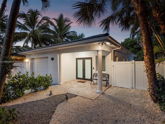 rear view of house featuring an attached garage, stucco siding, fence, and french doors