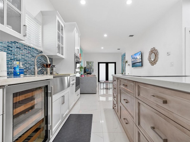 kitchen featuring wine cooler, light brown cabinets, white cabinets, decorative backsplash, and glass insert cabinets