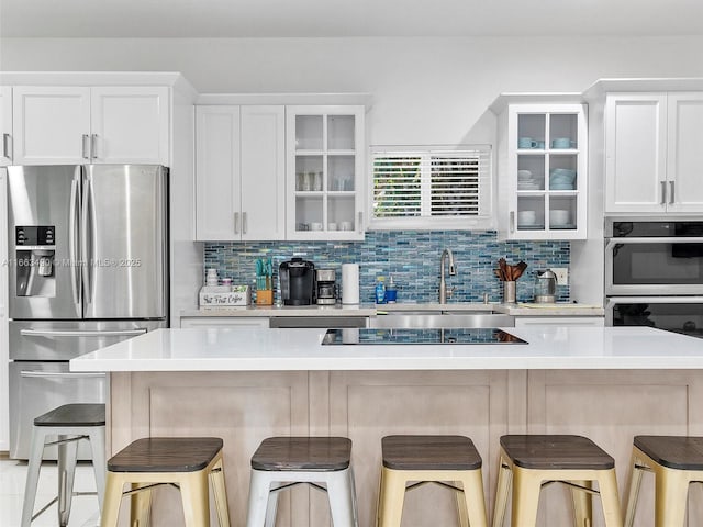 kitchen with a breakfast bar, white cabinets, light countertops, appliances with stainless steel finishes, and glass insert cabinets